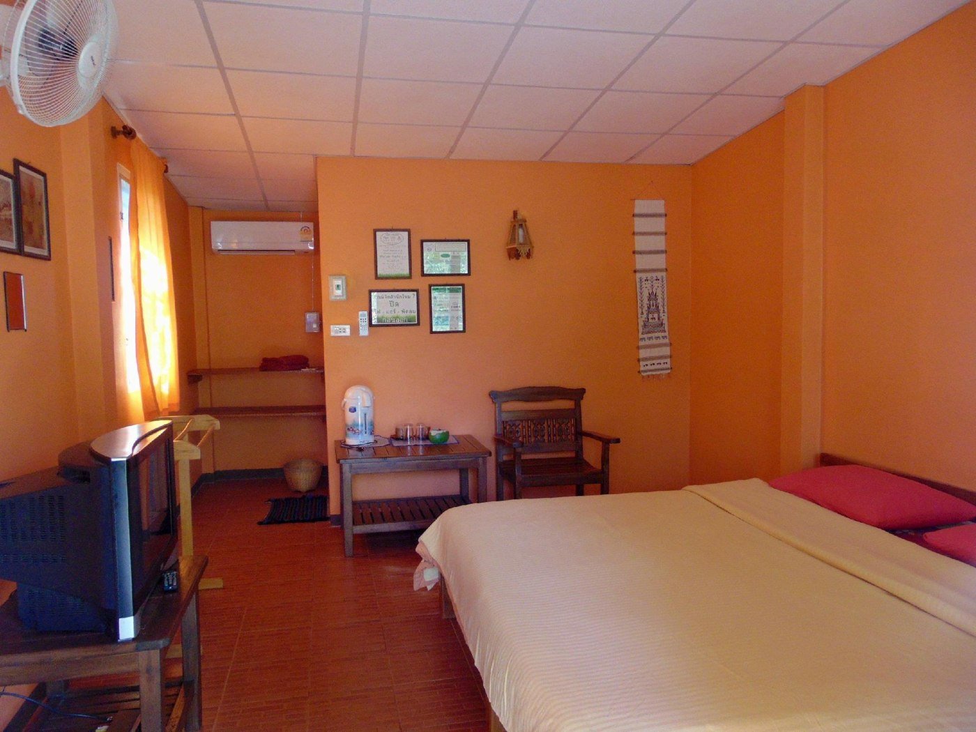 Orange-walled double bedroom with seating and television at Siam Garden Bungalows